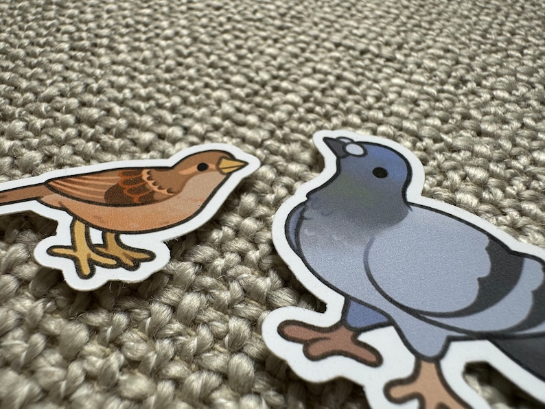 May include: Two cartoon bird stickers, one brown sparrow and one gray pigeon, on a beige textured background.