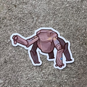 Op de afbeelding: Een gestanste sticker met een gestileerd, viervoetig wezen met een grote, hoekige, steenachtige kop en metalen, gesegmenteerde ledematen. Het wezen is gekleurd in tinten van gedempt paars en bruin, met een klein, helderblauw cirkelvormig accent op één poot.