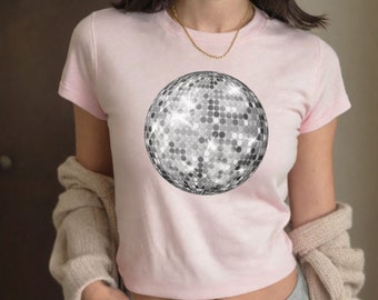 Puede incluir: Una camiseta rosa con un gráfico de bola de discoteca plateada. La camiseta es de estilo corto y tiene mangas cortas.