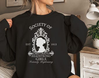 May include: Black sweatshirt with a white graphic design that says "Society of Obstinate Headstrong Girls Seriously Displeasing" with an illustration of a woman's profile in a decorative frame. The text "Est 1813" is also included.