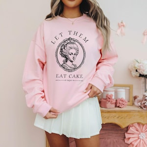 May include: Pink sweatshirt with a black and white illustration of a woman with the text "Let Them Eat Cake".