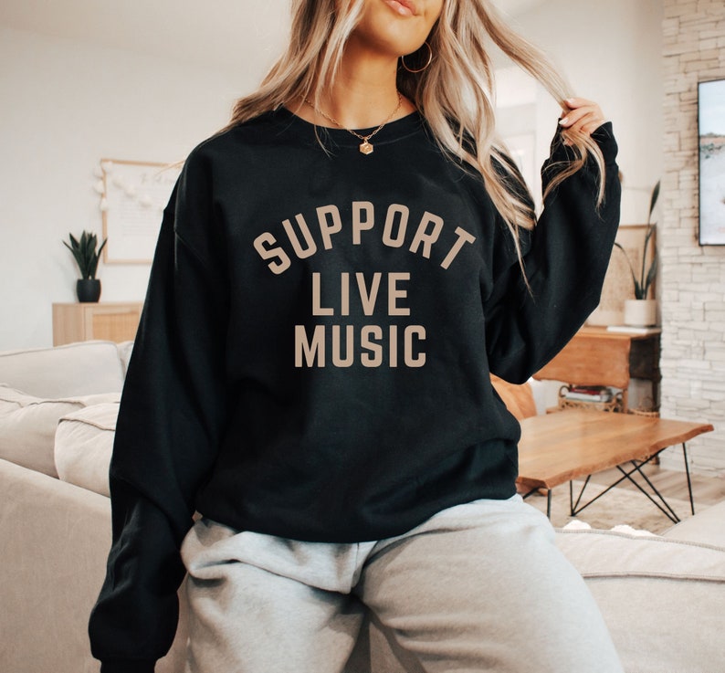May include: A black sweatshirt with the text "SUPPORT LIVE MUSIC" printed in beige on the front.