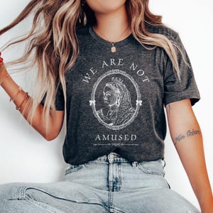 May include: A dark gray t-shirt with a white graphic of a queen with a crown and the text "We are not amused".