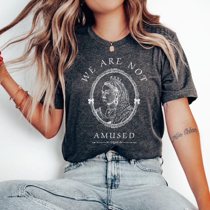 May include: A dark gray t-shirt with a white graphic of a queen with a crown and the text "We are not amused".