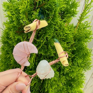 Op de afbeelding: Een set van drie keramische mokken met een gespikkelde, cr&egrave;mekleurige glazuur. Elke mok heeft een ander handgeschilderd ontwerp: een blauw en groen blad, een gele bloem en een rode bes. De mokken hebben een eenvoudig, modern ontwerp.