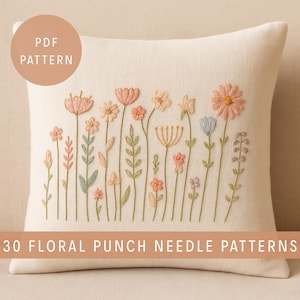 Op de afbeelding: Crèmekleurig vierkant kussen met geborduurd bloemmotief. De borduursels tonen verschillende bloemen in roze, perzik en geel, met groene stelen en bladeren. Tekst op het kussen luidt "PDF PATTERN" en "30 FLORAL PUNCH NEEDLE PATTERNS".