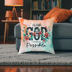 Könnte beinhalten: Quadratisches Dekokissen mit dem Text "With GOD All Things Are Possible" in Schwarz, umgeben von floralen Akzenten. Das Kissen hat einen Hintergrund im Aquarellstil mit orangefarbenen, grünen und weißen Farbtönen. Der Text "Matthew 19:26" steht unten.