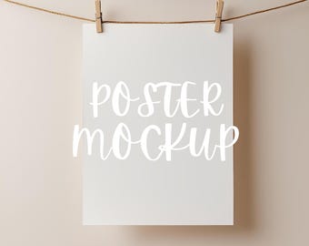 May include: A white poster mockup hanging from a string with wooden clothespins. The poster has the text "POSTER MOCKUP" written on it in white.