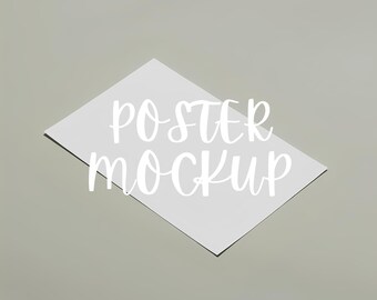 Puede incluir: Una maqueta de póster rectangular blanco con el texto "POSTER MOCKUP" en una fuente cursiva. El póster está en ángulo, con una sombra sobre un fondo gris claro.