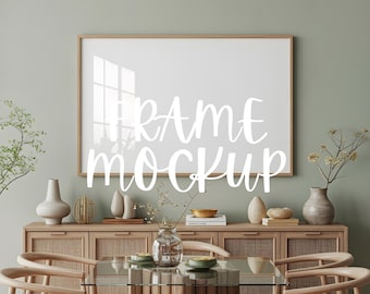 May include: A rectangular wall art mockup in a light wood frame, with the text "FRAME MOCKUP" in white script. The art hangs above a wooden cabinet with vases and a glass-topped table with chairs. The room has a neutral colour palette.
