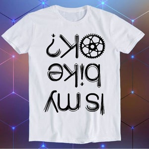May include: White t-shirt with black text that reads "Is This Bike Ok?" with a bicycle sprocket graphic above the text.