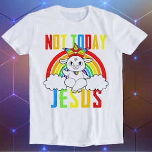 Puede incluir: Camiseta blanca con un arcoíris y una cabra de dibujos animados con cuernos y un pentagrama en la frente. El texto "NOT TODAY JESUS" está impreso en la camiseta.