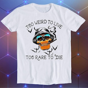 May include: White t-shirt with a skull wearing sunglasses and a hat, smoking a cigarette. The text "Too Weird To Live Too Rare To Die" is printed on the shirt.