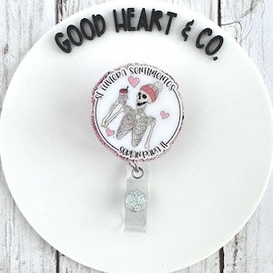 May include: A round badge reel featuring a skeleton wearing a beanie and holding a coffee cup. The badge has the text "Si tuviera sentimientos" and "Serian para ti" in a circular design with pink hearts.
