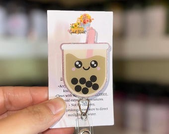 May include: A cute boba tea-themed badge reel with a smiling face and pink glitter accents. The badge reel is attached to a white card with the words "Good Heart" and care instructions. The reel has a clear plastic clip.