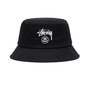 May include: Black bucket hat featuring a white logo. The hat has a wide brim and a rounded crown. The logo is a stylized script with a circle around the letter "S".