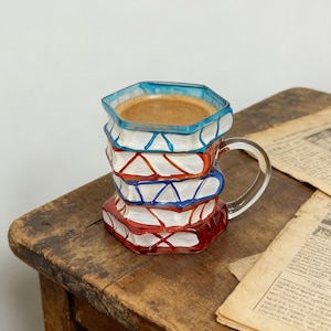 May include: A white ceramic mug with a black handle and the text "But First, Coffee" in a black, handwritten-style font. The mug is on a white surface.