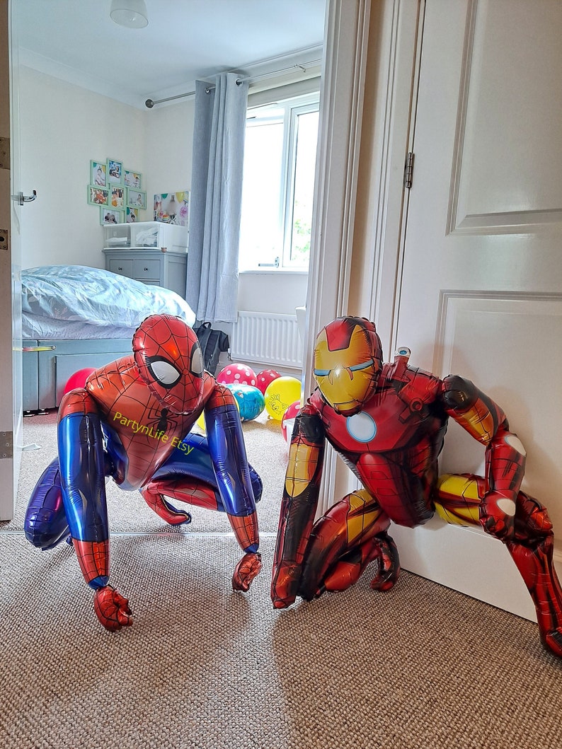 Puede incluir: Dos globos grandes de aluminio, uno rojo y otro azul, que representan a los superh&eacute;roes Iron Man y Spiderman. Los globos est&aacute;n en un suelo de moqueta en una habitaci&oacute;n con una puerta y una puerta blanca. El globo rojo est&aacute; parcialmente detr&aacute;s de la puerta. El globo azul tiene el texto "PartynLife Etsy".