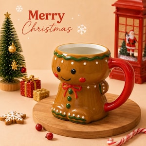 May include: A brown ceramic mug shaped like a gingerbread person with a red handle, green icing details, and a smiling face. The mug features white dots and a red bow. The text Merry Christmas is visible above the mug, along with snowflake icons.