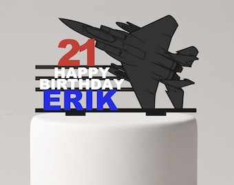 Puede incluir: Un adorno para tarta con la silueta negra de un avión de combate, el número 21 en rojo, el texto blanco HAPPY BIRTHDAY y el nombre ERIK en azul, dispuestos sobre barras horizontales negras sobre una tarta blanca.