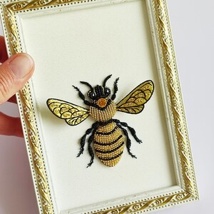 Embroidered wall art of a bee featuring intricate black and yellow embroidered wings.