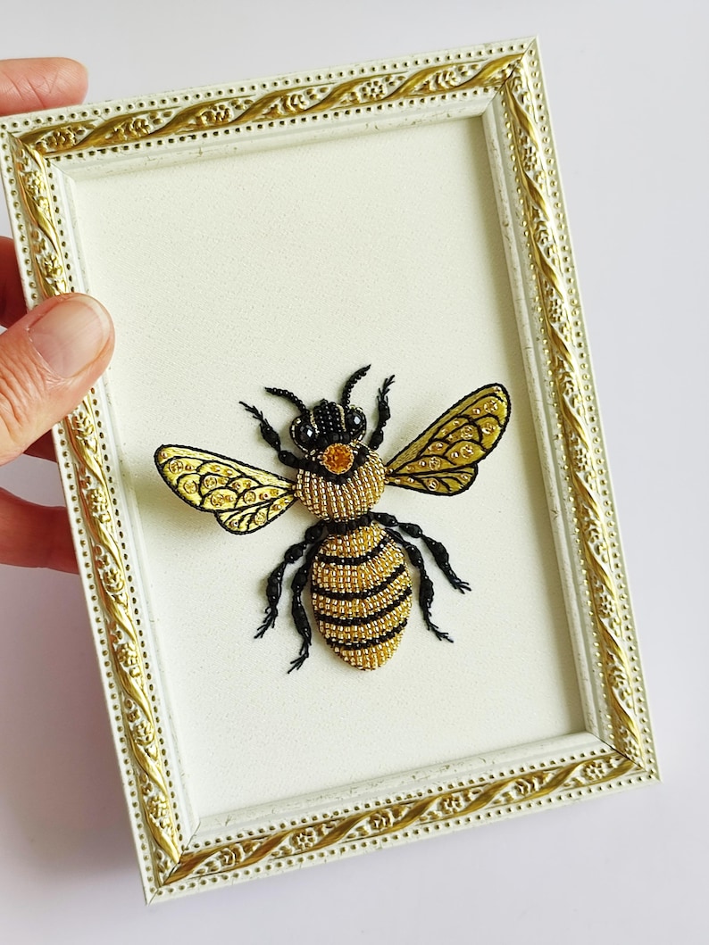 Embroidered wall art of a bee featuring intricate black and yellow embroidered wings.