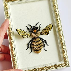 Close-up of a beaded wall hanging showcasing textured beadwork, gold beads, and glistening rhinestones forming a bee