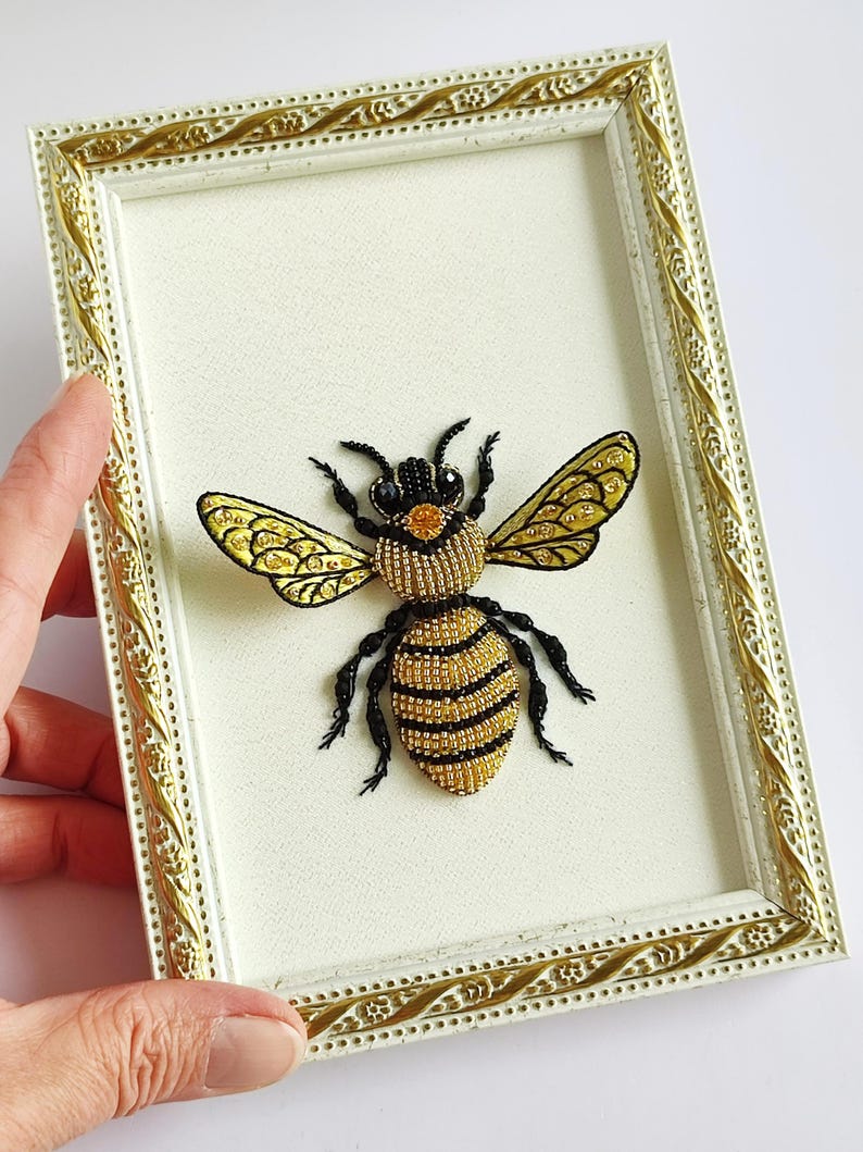 Close-up of a beaded wall hanging showcasing textured beadwork, gold beads, and glistening rhinestones forming a bee