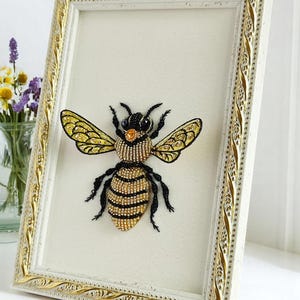 Bee wall decor in a light natural wood rectangular frame, styled on a clean white table surface.