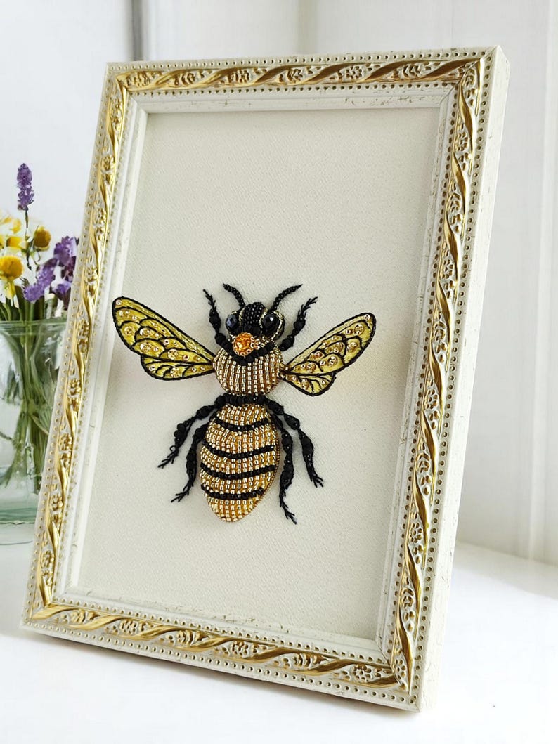Bee wall decor in a light natural wood rectangular frame, styled on a clean white table surface.