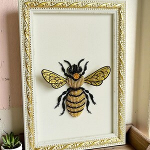 Honey bee decor piece with detailed black beaded legs and antennae, presented in a minimalist rustic frame.