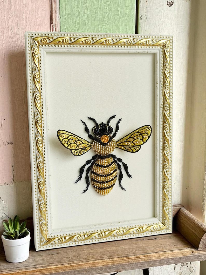 Honey bee decor piece with detailed black beaded legs and antennae, presented in a minimalist rustic frame.