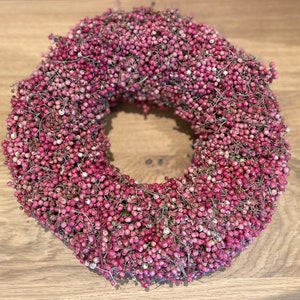 Könnte beinhalten: Ein Kranz aus rosa Pfefferkörnern, eine kreisförmige Anordnung von rosa Pfefferkörnern, eine beliebte Weihnachtsdekoration.