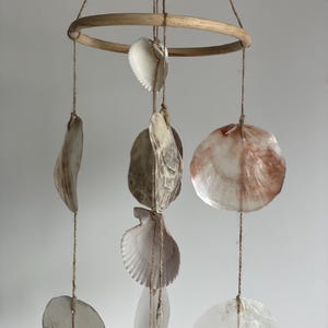 Peut inclure: Mobile de coquillages suspendu à un anneau en bambou naturel. Il présente divers coquillages blancs, beiges et roses, suspendus par de la ficelle. Cette décoration est conçue pour une utilisation en intérieur.