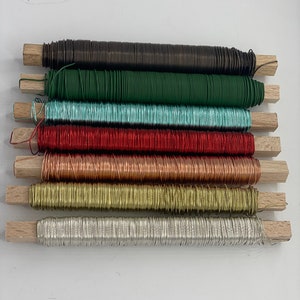 May include: Assortment of eight spools of floral wire in various colors, including brown, green, teal, red, copper, gold, and silver. The wire is wrapped around wooden dowels.