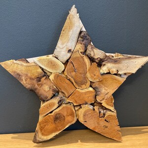 Può includere: Una grande stella di legno fatta di molti pezzi di legno di deriva. La stella è di colore marrone chiaro e ha un aspetto naturale e rustico.