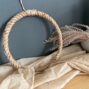 Könnte beinhalten: Ein natürlicher Jute-Seilkranz, perfekt, um Ihrer Wohnkultur einen rustikalen Touch zu verleihen. Der Kranz ist aus dickem, natürlichem Juteseil gefertigt und ist eine einfache, aber elegante Möglichkeit, Ihrer Wohnung einen Hauch von Natur zu verleihen.