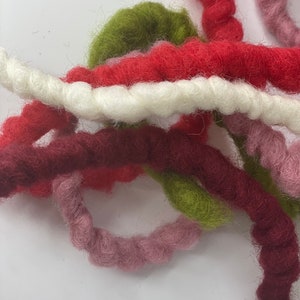 May include: A collection of colourful yarn strands in shades of red, white, green, burgundy, and pink. The yarn is soft and fluffy, perfect for crafting.