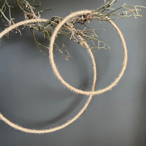 Puede incluir: Dos coronas de cuerda de yute natural colgadas en una pared gris oscuro. Las coronas están hechas de cuerda de yute natural gruesa y son perfectas para agregar un toque rústico a cualquier espacio.