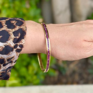 Op de afbeelding: Een gouden armband met een dunne band van roze edelstenen.