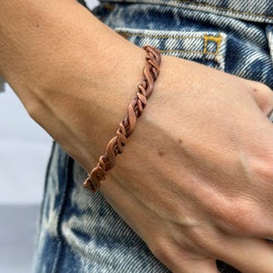 May include: A copper bracelet with a twisted design. The bracelet is worn on a person's wrist.