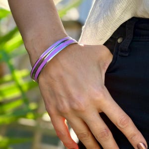 May include: A pair of silver bangles with a purple enamel stripe on each. The bangles are worn on a person's wrist.