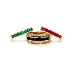 May include: Three gold rings with different colored gemstones. The top ring has a row of emerald green gemstones, the middle ring has a row of sapphire blue gemstones, and the bottom ring has a row of ruby red gemstones.