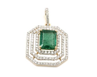 May include: A gold pendant featuring a large, rectangular emerald center stone. The emerald is surrounded by multiple layers of small, sparkling diamonds, creating a layered, geometric design. The pendant has a loop for a chain.