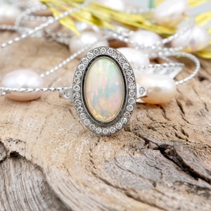 May include: A silver ring with a large oval opal gemstone surrounded by a halo of smaller diamonds.