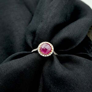 May include: A ring with a large, faceted ruby gemstone surrounded by a halo of smaller diamonds. The ring is set in white gold and has a polished finish.