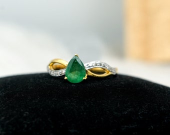 May include: A gold ring with a pear-shaped emerald gemstone and a band of small diamonds.