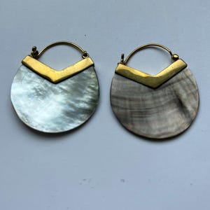 Puede incluir: Un par de pendientes de aro de oro con un diseño de concha y chevron dorado.