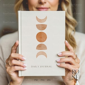 A lifestyle photograph of a woman softly smiling while holding a blank, cream-colored A5 hardcover book directly in front of her. She is holding the book with both hands, showcasing a delicate rose gold watch and rings. The lighting is soft and natural, creating a feminine, high-end aesthetic.