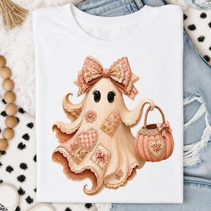 Peut inclure: Un t-shirt blanc avec un motif représentant un fantôme beige orné d'un grand nœud à motifs sur la tête. Le fantôme est décoré de divers patchs floraux et à carreaux et tient un panier rose en forme de citrouille avec un petit nœud assorti.